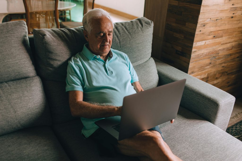 pexels-photo-27086257-27086257 | Modern Healthy Senior man in blue polo shirt using a laptop while sitting on a cozy couch indoors.
